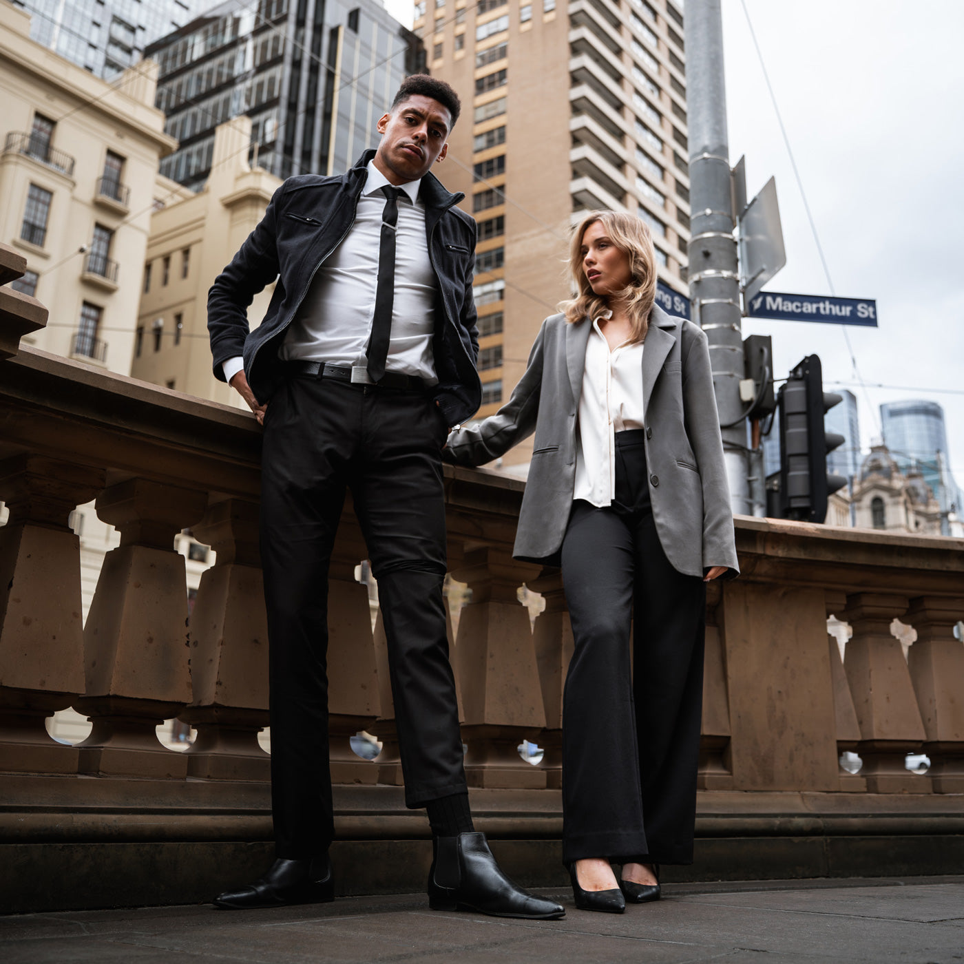 Mann im Business-Look mit schwarzen Businesssocken von BLACKSOCKS neben Frau im Hosenanzug in der Stadt.